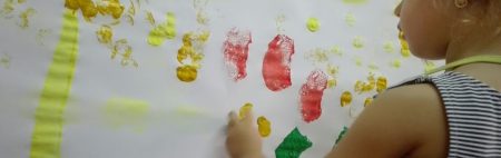 niña pintando con manos en papel blanco pared