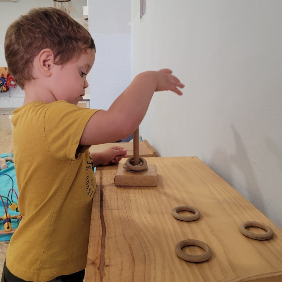 niño jugando en mesa metiendo anillas de madera en palo de madera